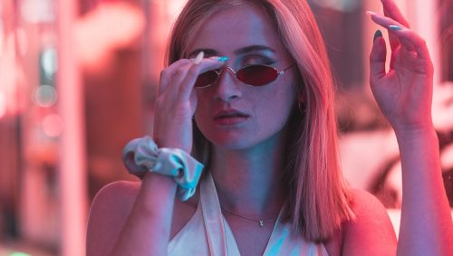 Jeune femme blonde sous les lumières colorées d’une fête foraine.