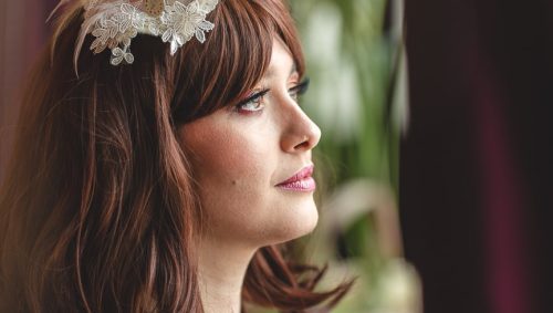Portrait d'une femme brune, son regard rêveur tourné vers la lumière, coiffée d'un ornement fleuri et vêtue d'une robe noire délicate, les mains croisées sur la poitrine.