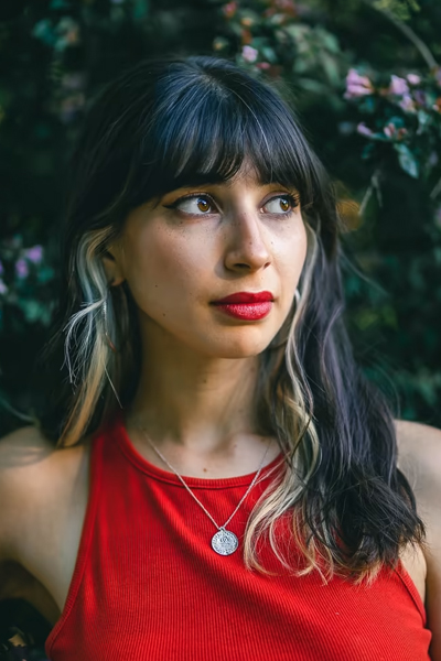 Femme avec une tenue rouge saturé et un arriere plan de buisson vert sombre, illustrant l'usage de couleurs complémentaire (rouge et vert)