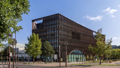 Façade moderne de la Maison de l'Innovation à Nantes, caractérisée par des lignes verticales sombres et des ouvertures en arc de cercle, sous un ciel bleu clair.