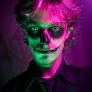 Homme maquillé façon Dia de los Muertos sous des lumières violettes et verte.