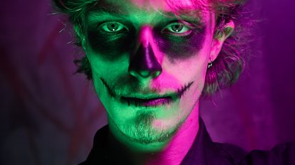 Homme maquillé façon Dia de los Muertos sous des lumières violettes et verte.