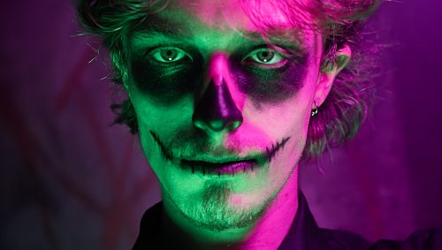 Homme maquillé façon Dia de los Muertos sous des lumières violettes et verte.