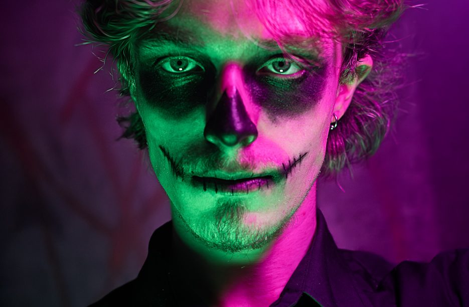 Homme maquillé façon Dia de los Muertos sous des lumières violettes et verte.