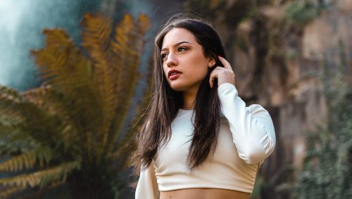 Jeune femme en blanc posant devant une cascade dans un parc.