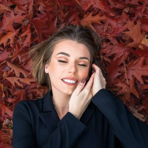 Femme souriante allongée sur des feuilles rouges d’automne.