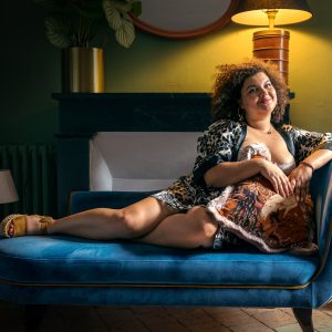 Dans une location airbnb, une femme est allongée sur une méridienne en velours bleu et porte un kimono à fleurs noire et blanche. L'éclairage tamisé, crée une scène chic. Le décor ajoutent une touche de sophistication.