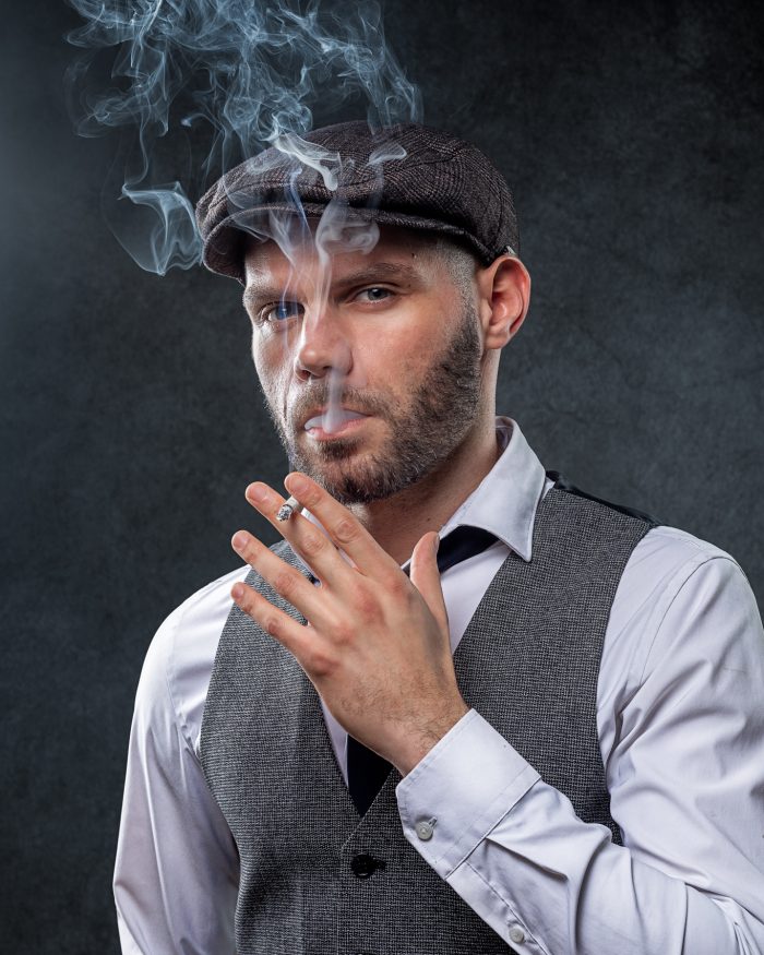 portrait en studio à Nantes : photo d'un homme portant une casquette de style Peaky Blinders, tenant une cigarette et regardant fixement l'objectif avec une expression sérieuse.