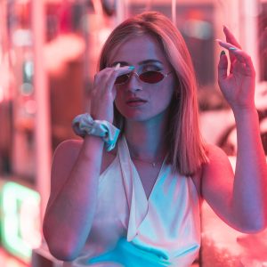 Jeune femme blonde sous les lumières colorées d’une fête foraine.