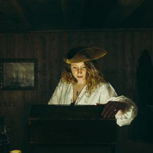 Dans un escape game une jeune femme en costume de pirate, concentrée et penchée sur un coffre illuminé par une lumière mystérieuse.