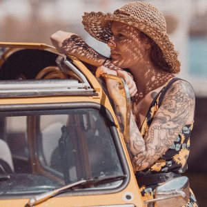 Portrait vintage d'une femme en robe fleurie appuyée sur une 2CV jaune.