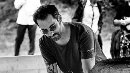 Un verrier concentré manipule une tige près d'un four, son visage reflétant l'attention portée à son métier d'art. 