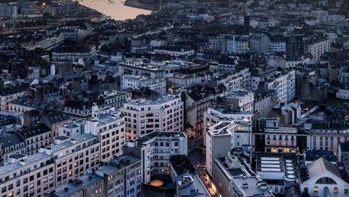 Vue aérienne de Nantes au crépuscule, avec la Loire divisant la ville et un ciel orangé nuageux. 