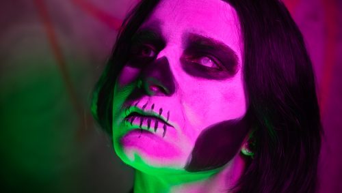 Portrait d'une personne avec un maquillage de squelette travaillé, illuminée par des lumières vertes et roses pour une ambiance d'Halloween.