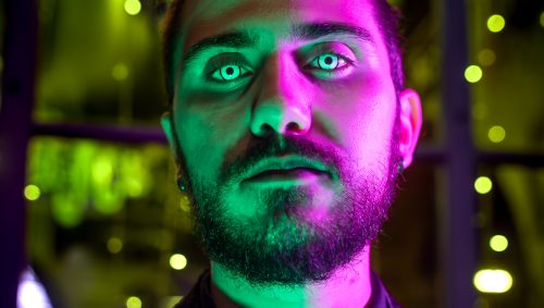Portrait d'un homme en costume et cravate avec des lentilles de contact blanches, sous un éclairage vert et violet pour Halloween.
