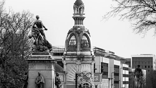 Monument aux morts de Nantes en noir et blanc avec des statues, La tour LU et des passants, le tout dans un style architectural unique. 