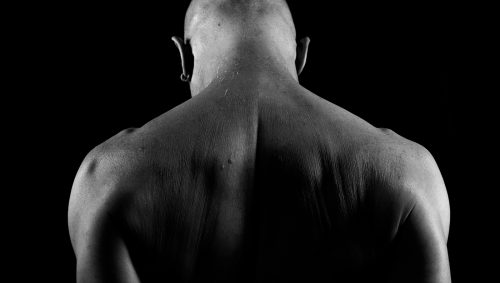 Portrait en noir et blanc du dos et de la nuque d'un homme chauve, éclairés de côté, sur fond noir.