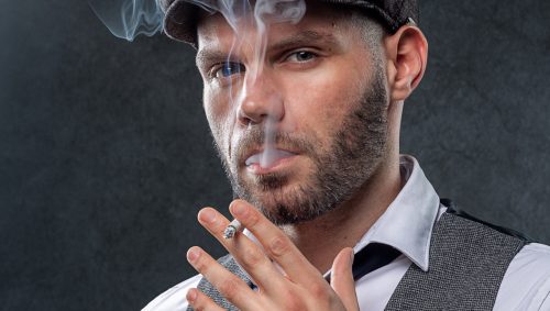 Portrait créatif en studio d’un homme avec une casquette gavroche, fumant une cigarette avec un regard intense.
