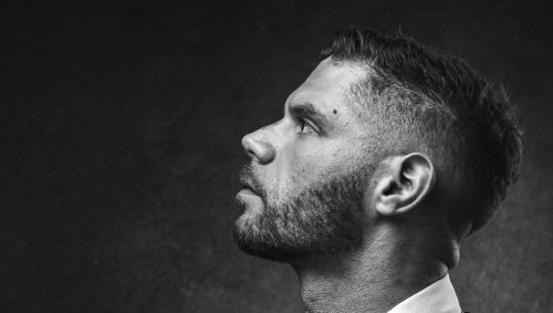 Portrait en noir et blanc d'un homme au style Peaky Blinders, le regard déterminé vers le haut.